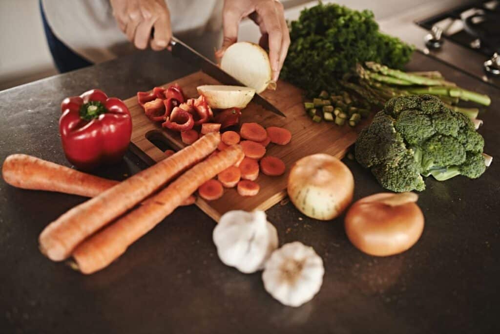 Hands cutting vegetables on chopping board.