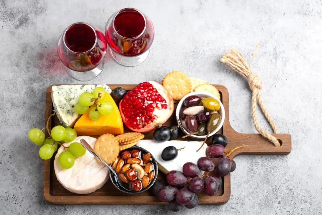 A charcuterie board with mixed of snacks, fruits, and wine.