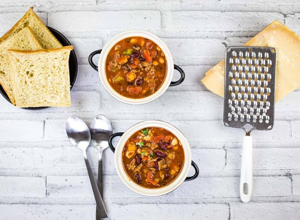 A top down shot of Pasta e Fagioli Soup with cheese and bread.