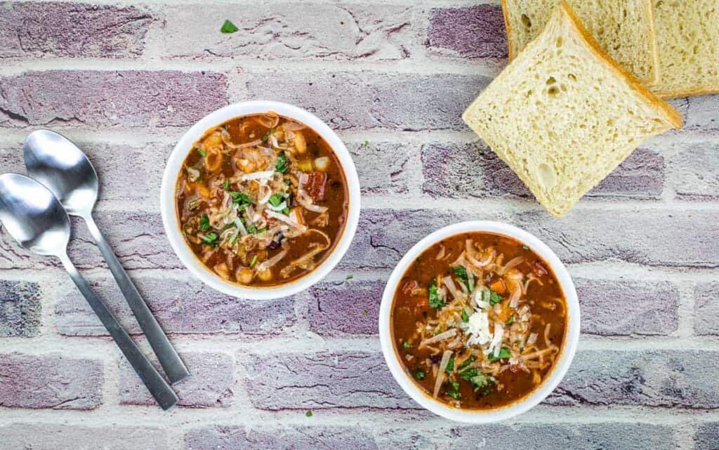 A top-down shot of two bowls of Pasta e Fagioli Soup with bread nearby.