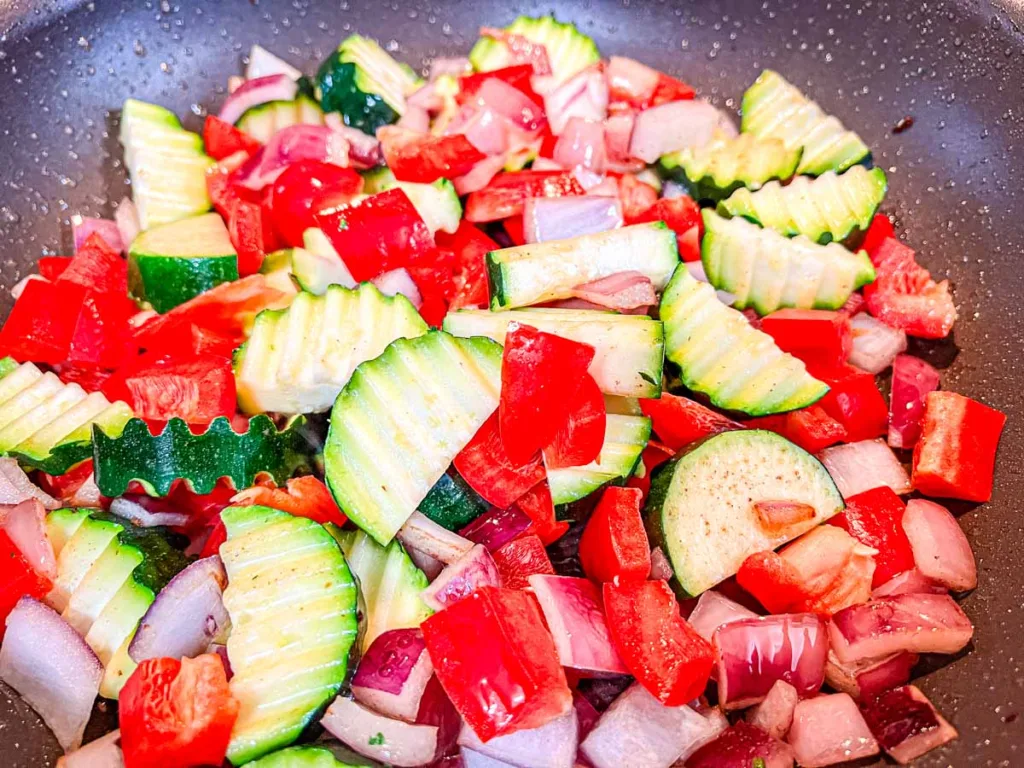 Zucchini and peppers added to onions in a skillet.