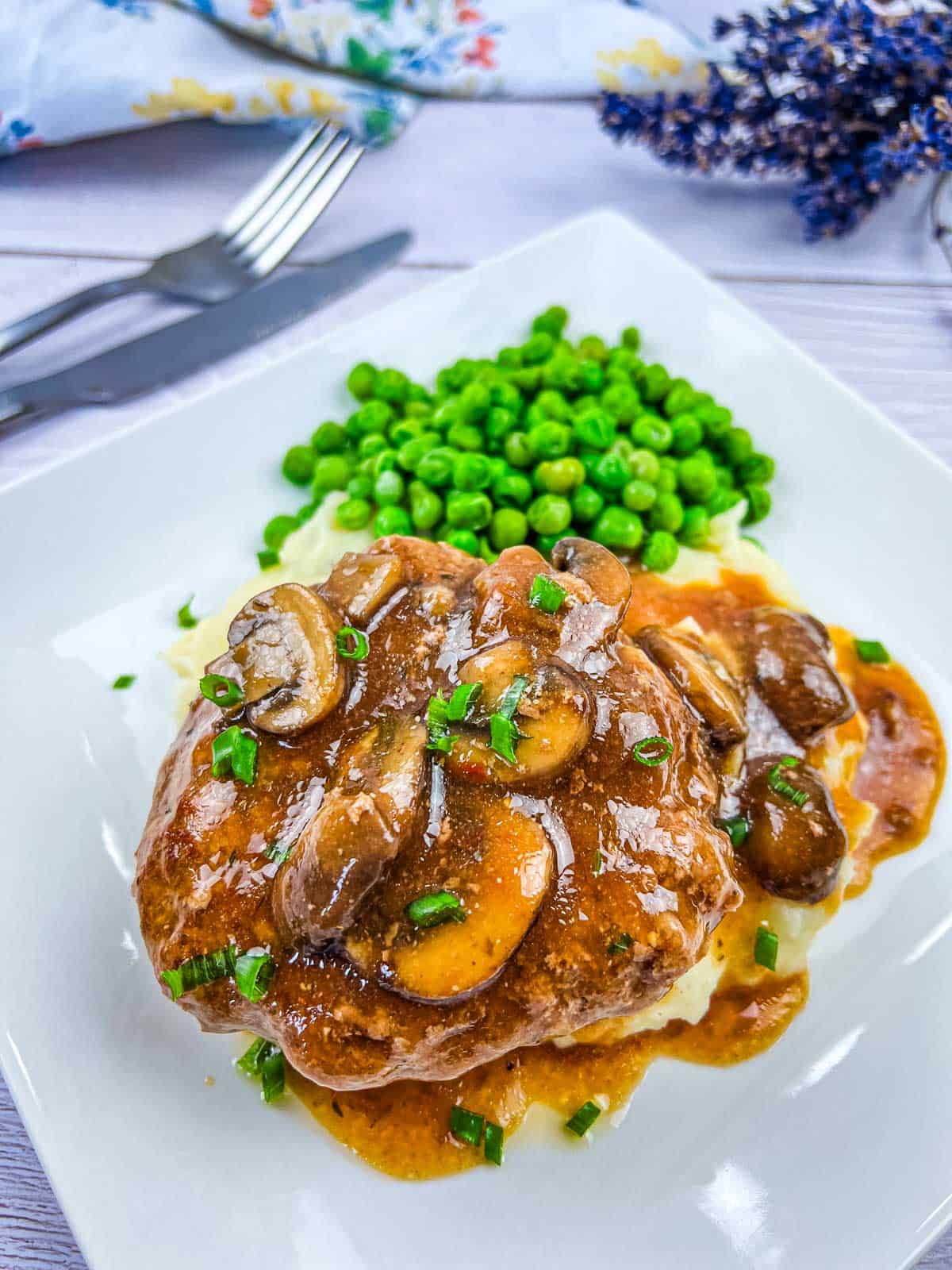 Diner-style Salisbury Steak on a white plate with peas.