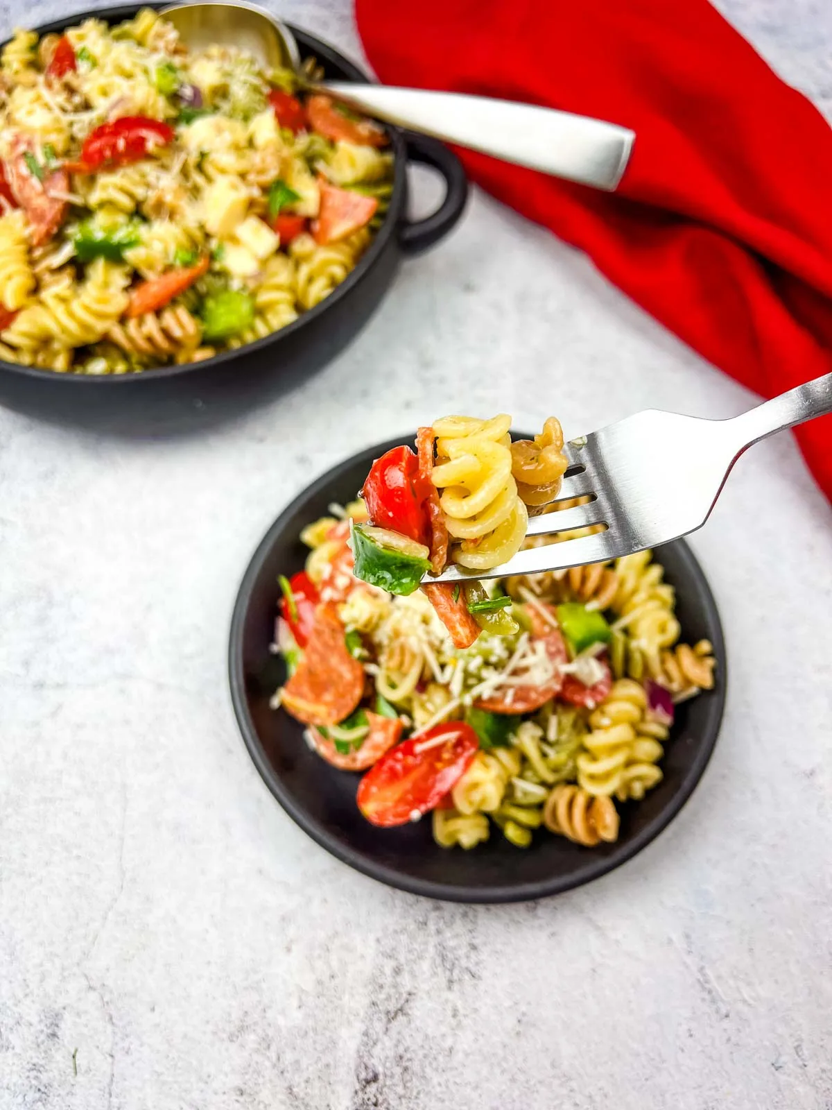 A fork holding Pizza Pasta Salad with bowls of salad in the background.