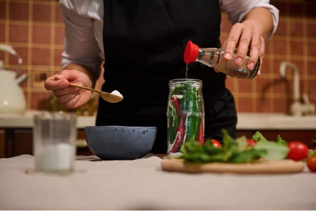 Pouring vinegar into a jar filled with different ingredients. 