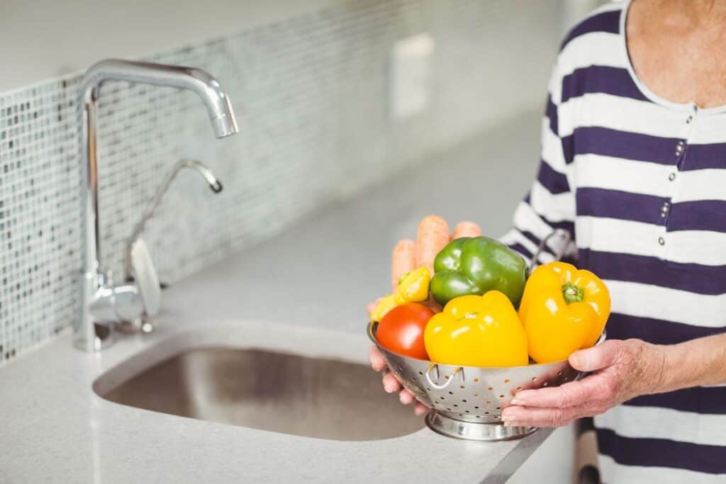 Woman holding a metal colander with veggies on it.