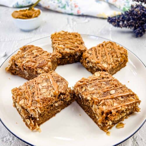 Biscoff Cookie Butter Steusel Bars on a white plate with a bowl of cookie butter in the background.