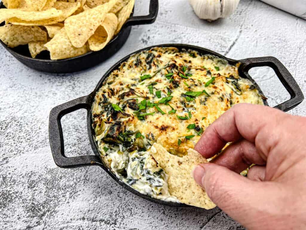 A hand dipping a chip into a Copycat Applebee's Spinach Artichoke Dip.