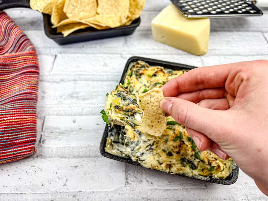 A hand holding a chip dipped in Copycat Applebee's Spinach-Artichoke Dip.