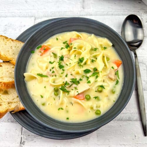 A bowl of Creamy Chicken Noodle Soup topped with chopped parsley.