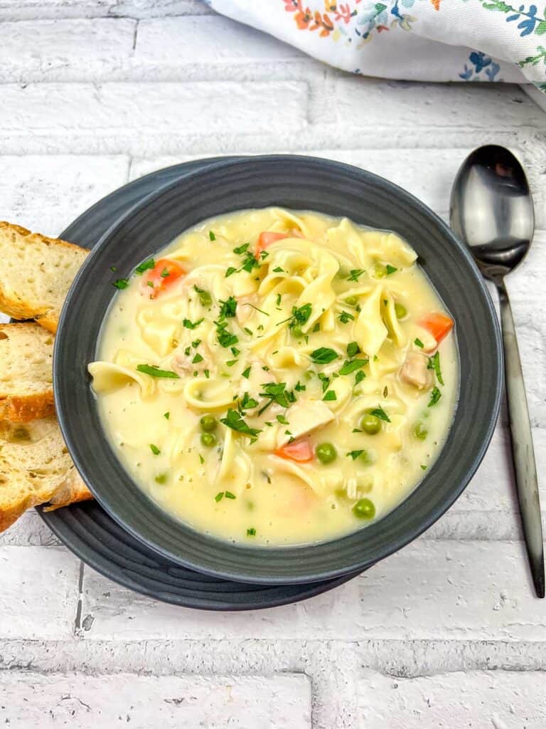 A bowl of Creamy Chicken Noodle Soup topped with chopped parsley.