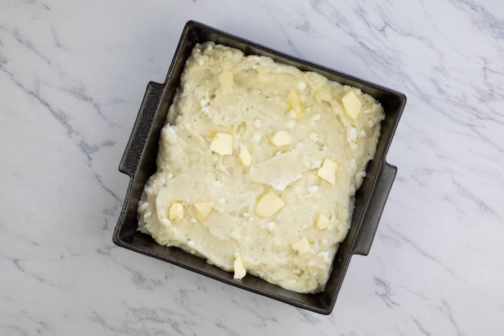 Mashed potatoes dotted with butter in a baking dish.