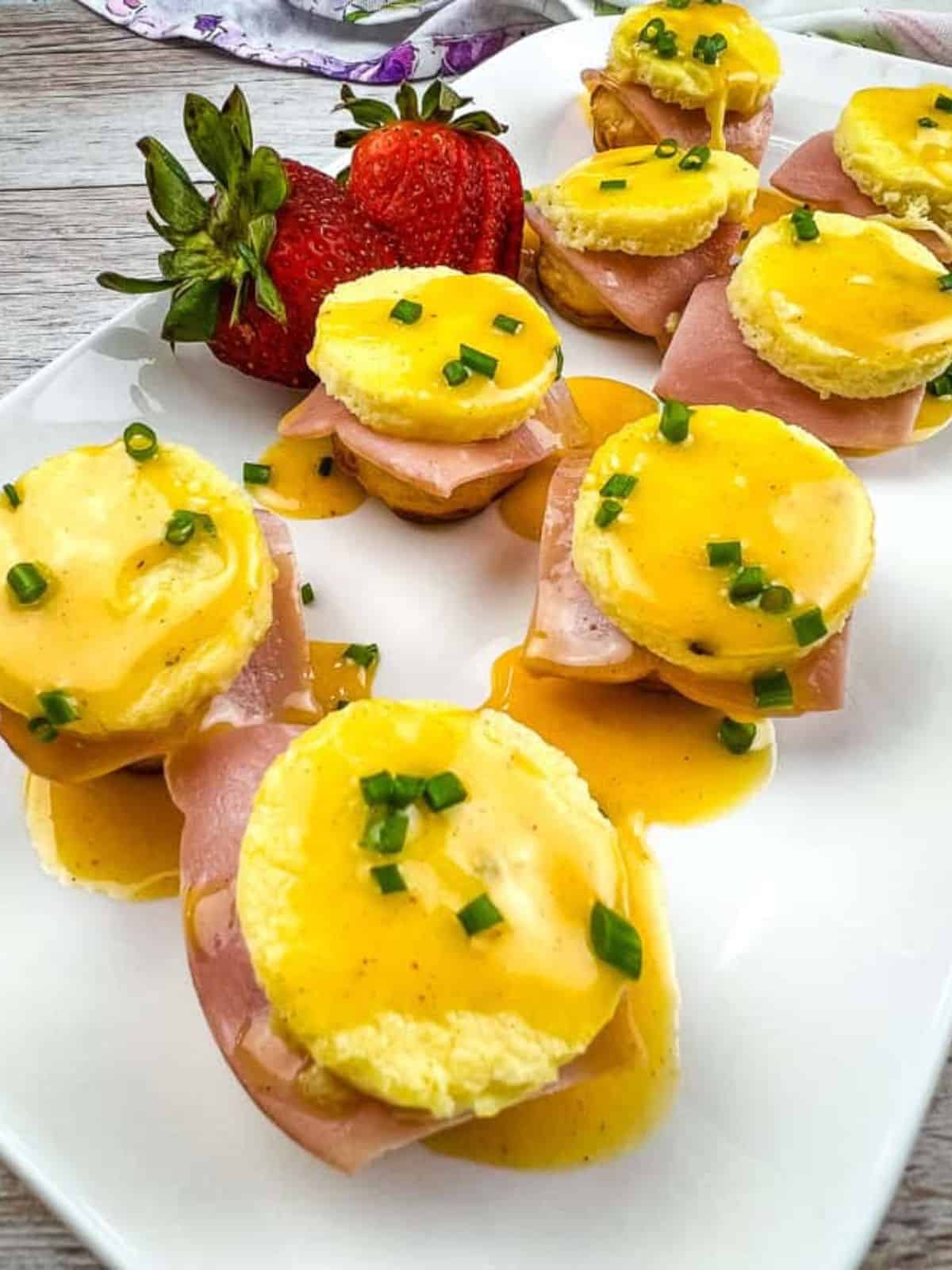 Eight pieces of Egg Benedict Bites on a white plate with strawberries.