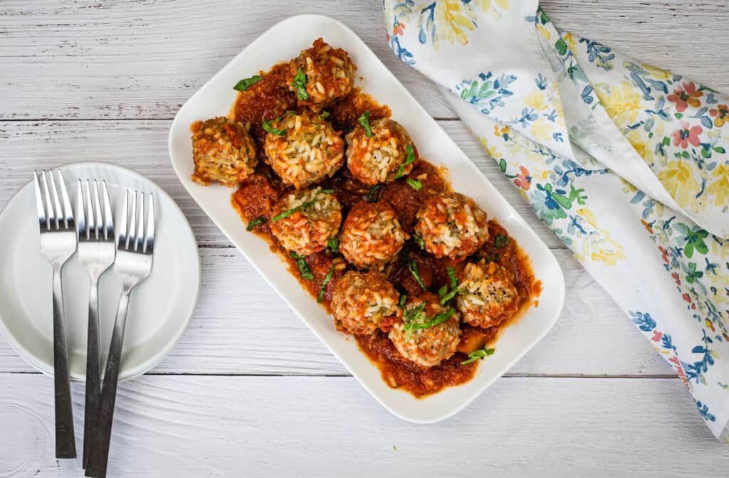 Slow Cooker Porcupine Meatballs on a white plate with three forks on the left side.