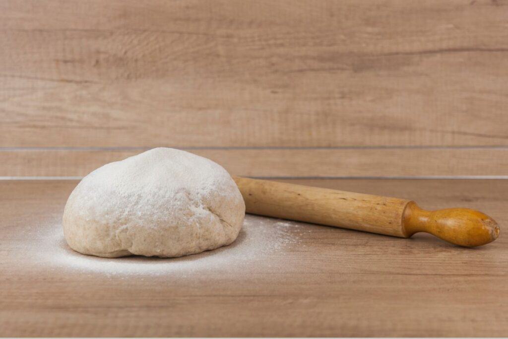 Homemade pizza dough with rolling pin on the wooden table.