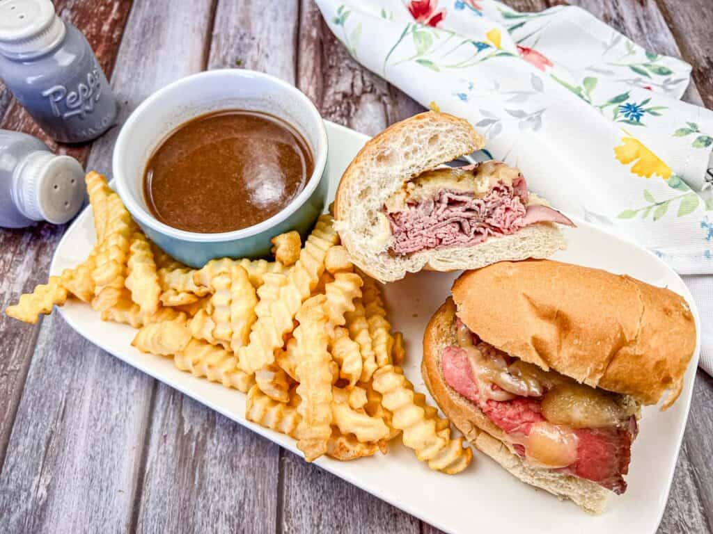 Sliced of Copycat Cole's French Dip Sandwich with fries and dip on a white plate.