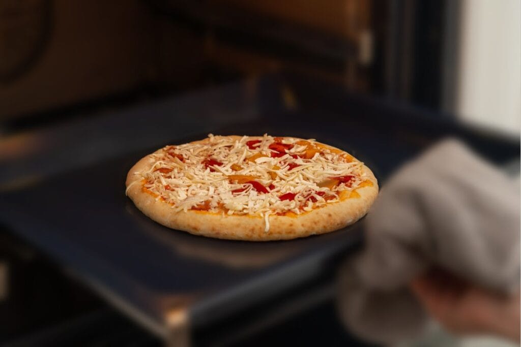 View of a raw pizza in front of an oven.