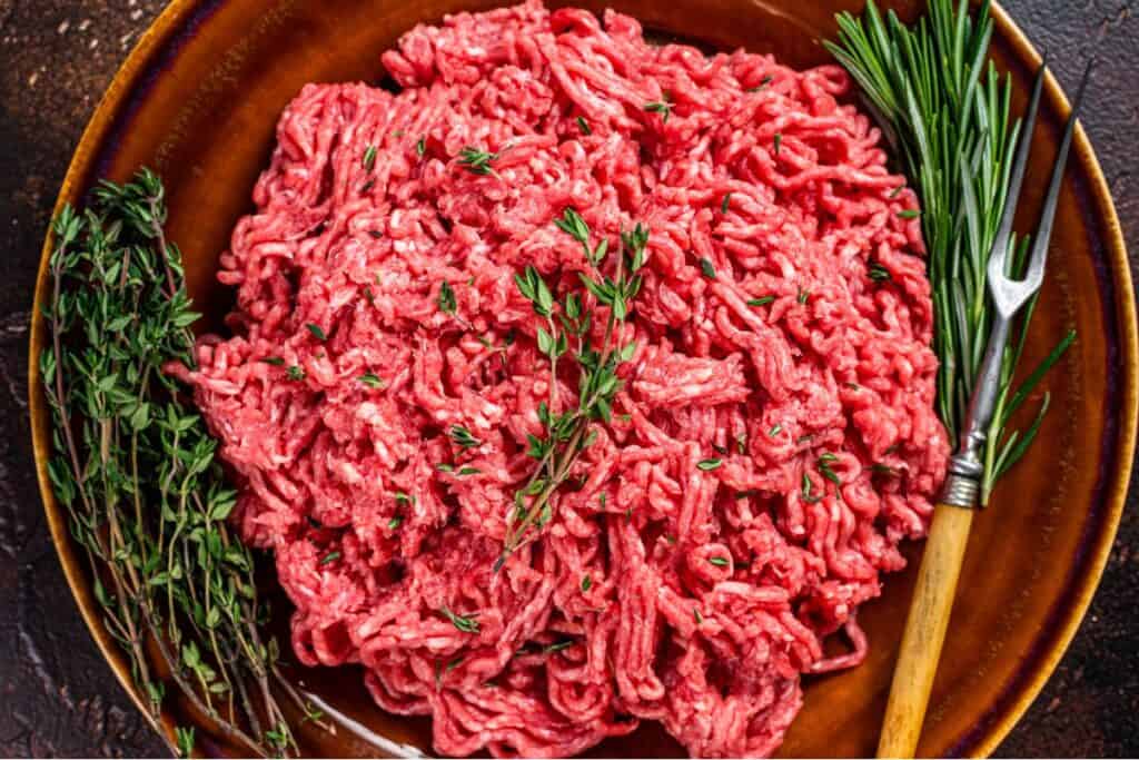 Raw ground beef on a rustic plate with herb.