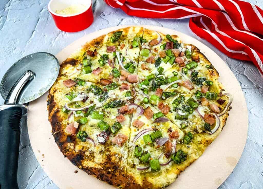 Ham and asparagus pizza with a pizza cutter nearby.