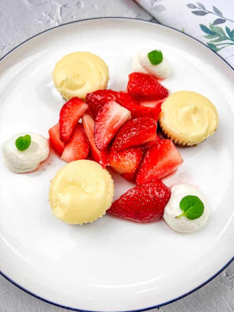 A white plate with strawberries and mini biscoff cheesecakes.