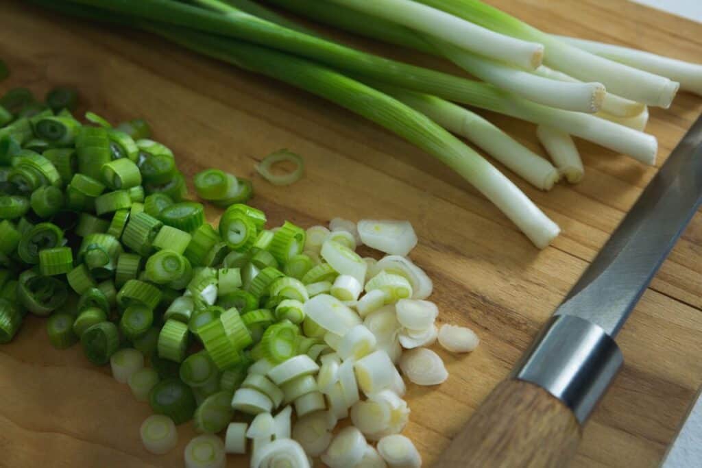 Close-up of chopped scallions with knife on chopping board,