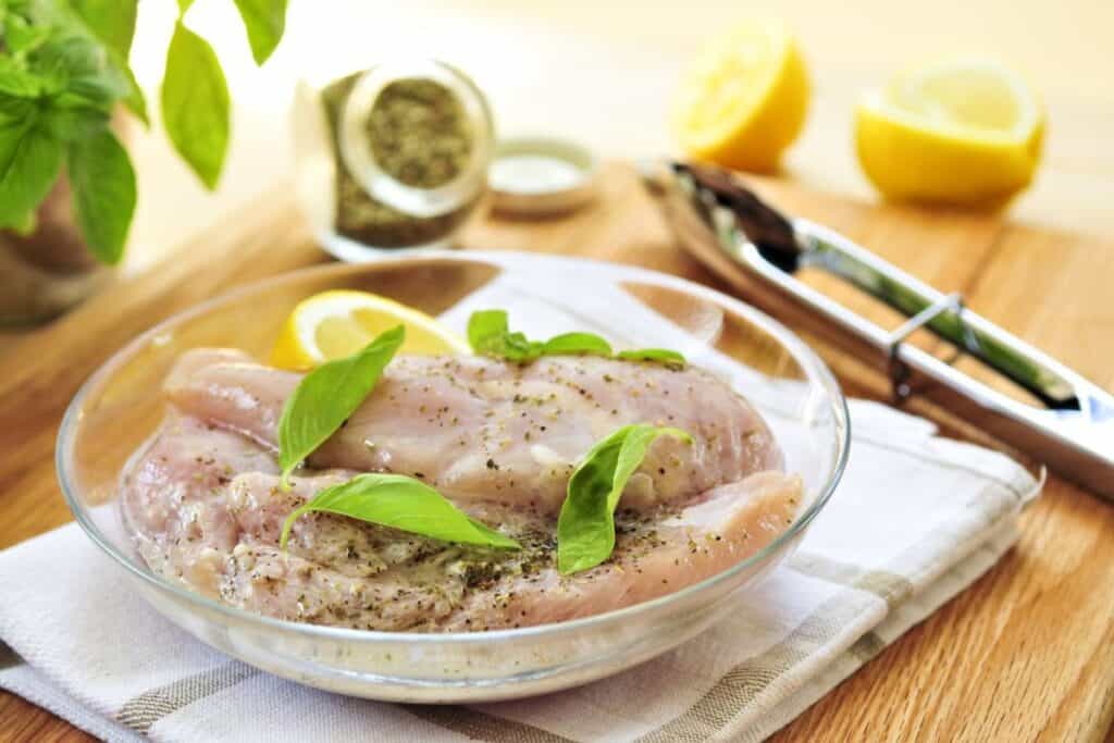 Marinating raw chicken breasts in lemon juice and herbs.