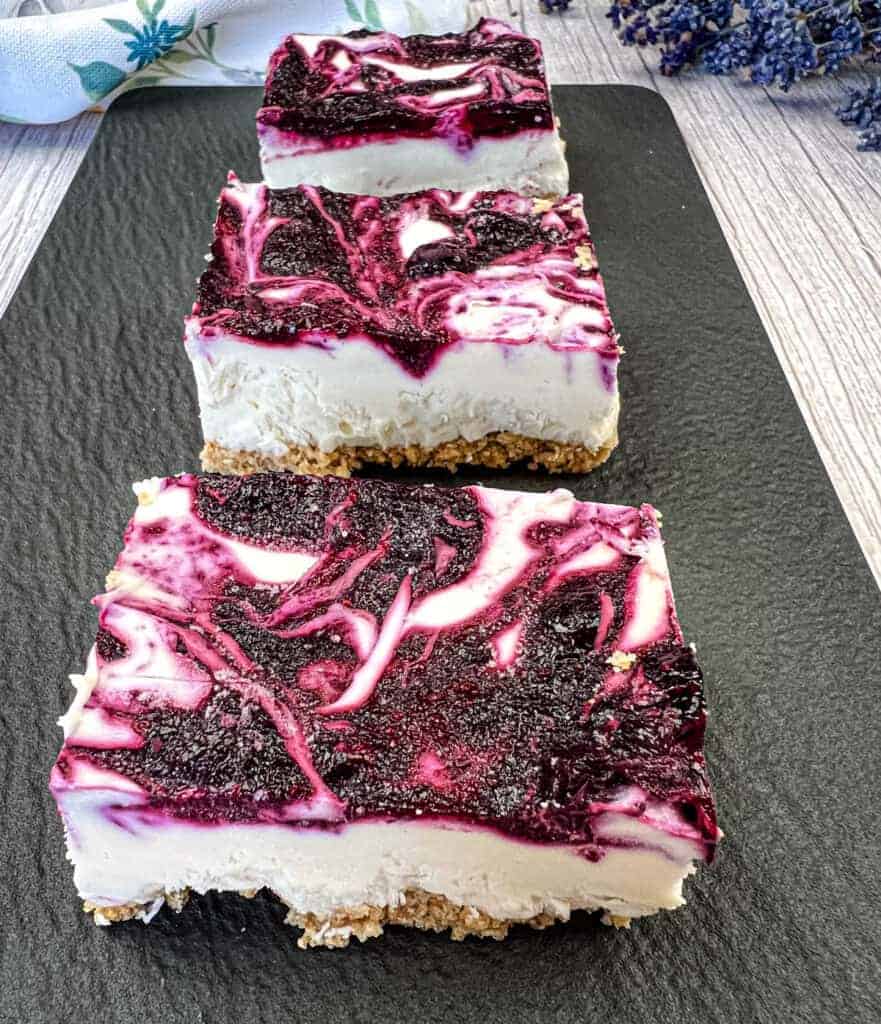 Three pieces of No-Bake Blueberry Cheesecake Bars on a black slate plate.