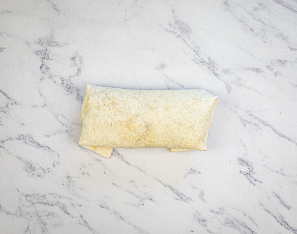 Fold the sides of the tortilla over the filling and roll it up tightly to form a burrito.