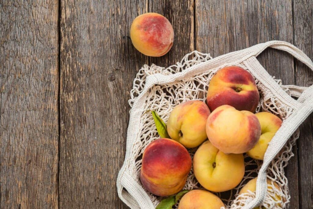 Ripe peaches in eco bag on wooden background.