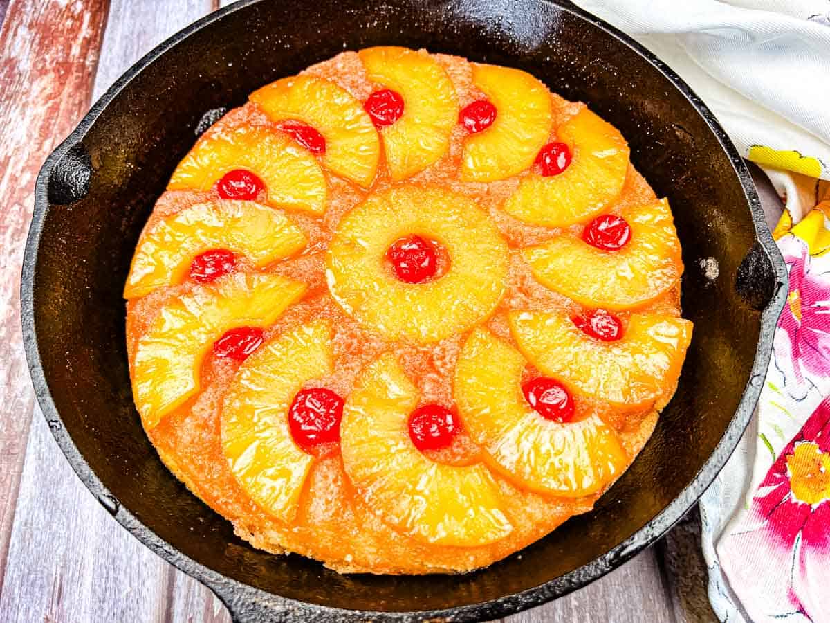 A pineapple upside-down cake with cherry toppings in a cast iron skillet.