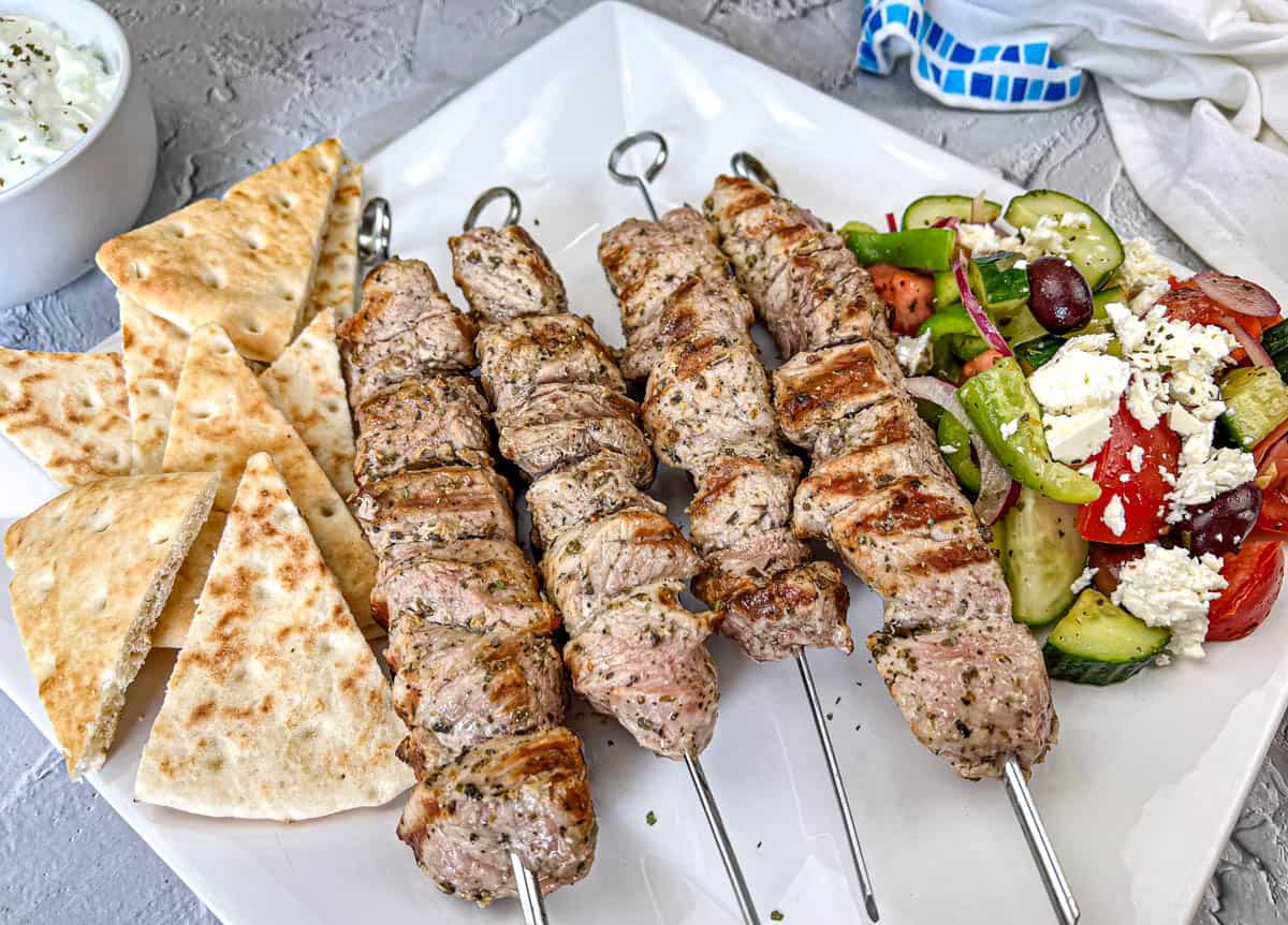 Ninja Woodfire Pork Souvlaki with Horiatiki Salad and pita bread on a white plate.