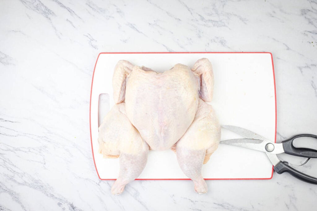 Whole raw chicken on a cutting board with kitchen shears.