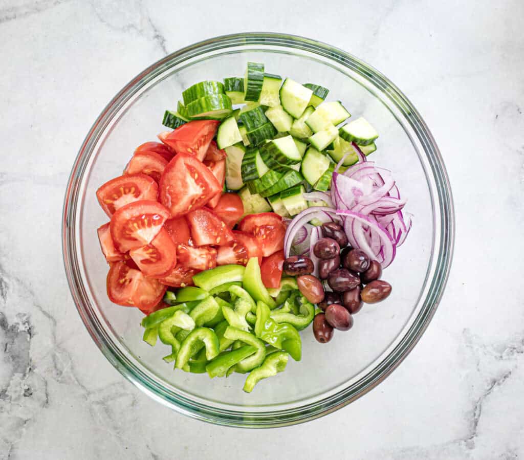 Mix tomatoes, cucumber, bell pepper, red onion, and Kalamata olives in a large salad bowl.