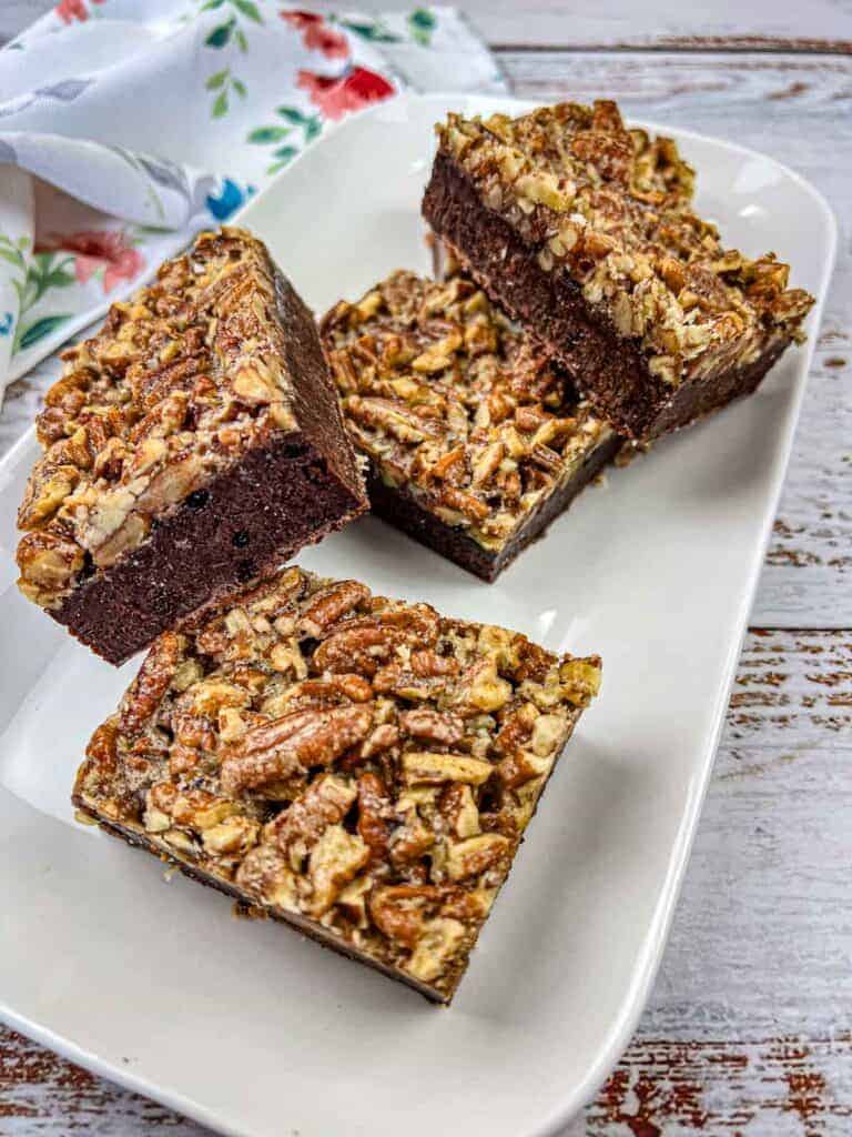 A close-up of two pecan brownies on a slate surface, showing the rich, chocolatey interior and a topping of chopped pecans.