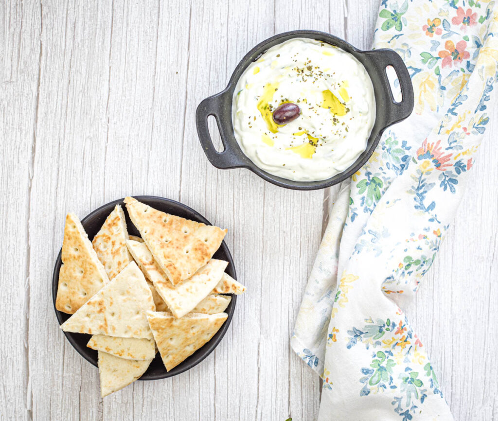 Top-down shot of Tzatziki Sauce paired with triangular pita on a bowl.