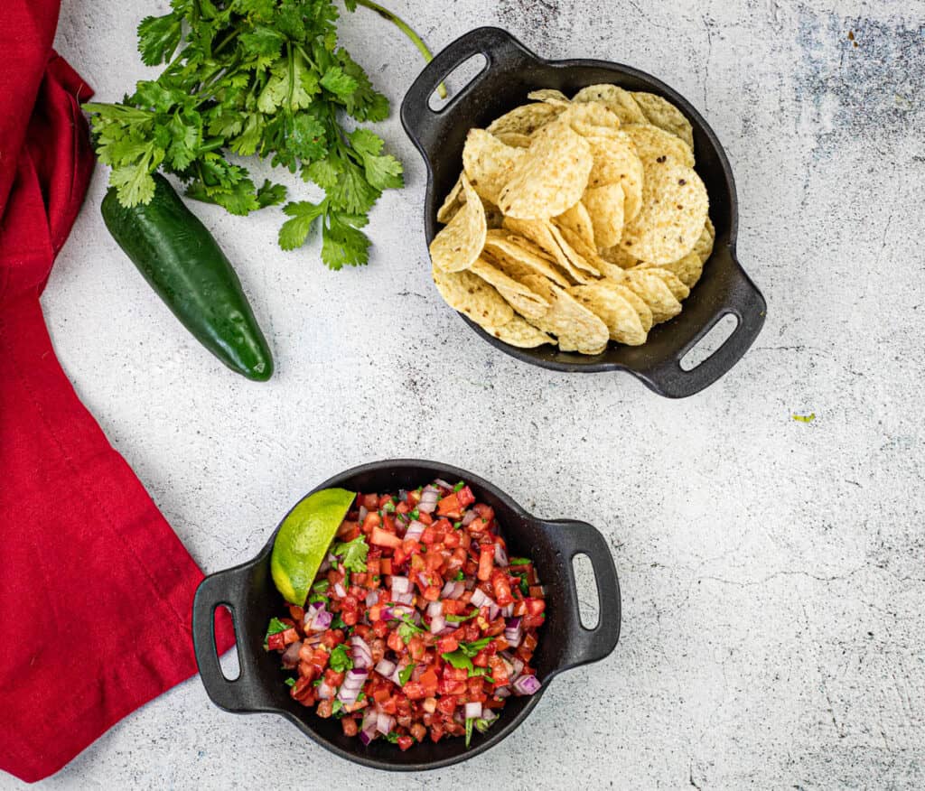 Top-down shot of Pico de Gallo on a black cast iron bowl beside the chips.