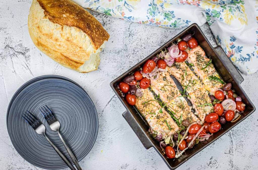 Top-down shot of Greek Salmon on a pan, with bread and plates besides.