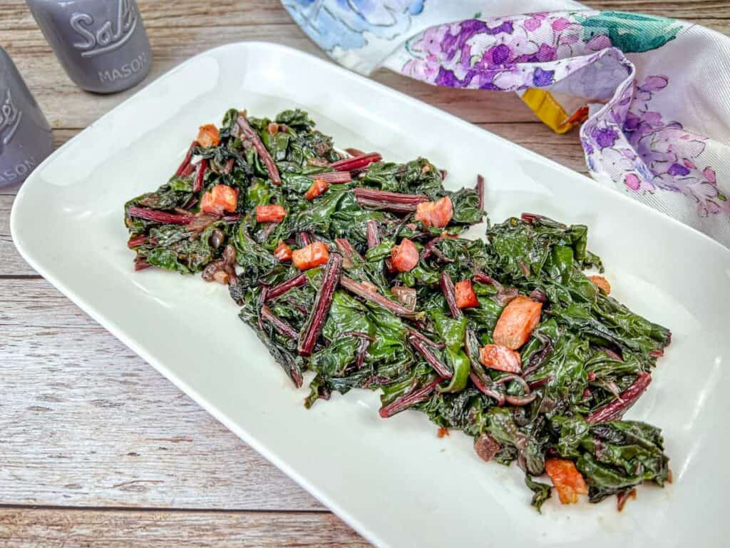 Sauteed Beet Greens with Pancetta served on a white plate.