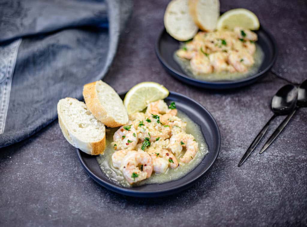 Shrimp scampi with a slice of lemon and bread on a plate.