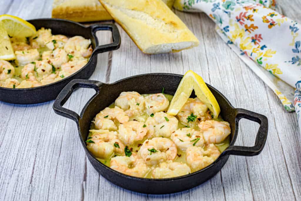 Shrimp scampi with a slice of lemon on a black dish.