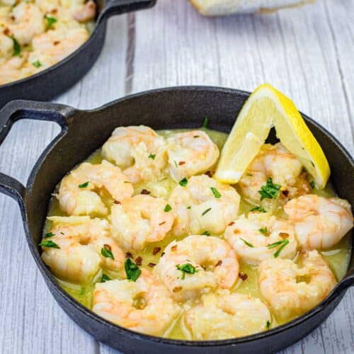 Shrimp scampi with a slice of lemon on a black skillet.