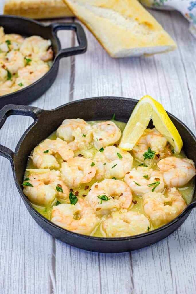 Shrimp scampi with a slice of lemon on a black skillet.