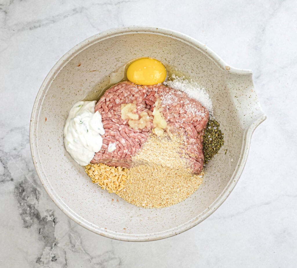 "Combine ground meat, bread crumbs, egg, tzatziki sauce, garlic, onion flakes, mint, oregano, salt, and pepper in a large bowl.