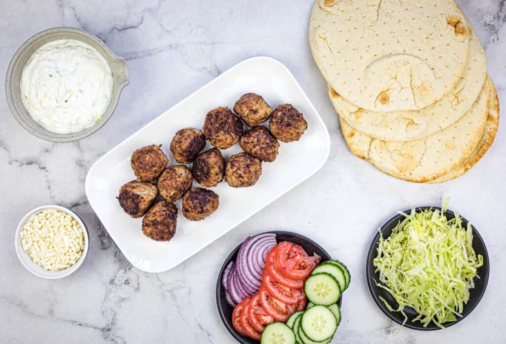 Top bread with 2 tablespoons tzatziki, 4 meatballs, lettuce, cucumber, red onion, tomato, and feta.