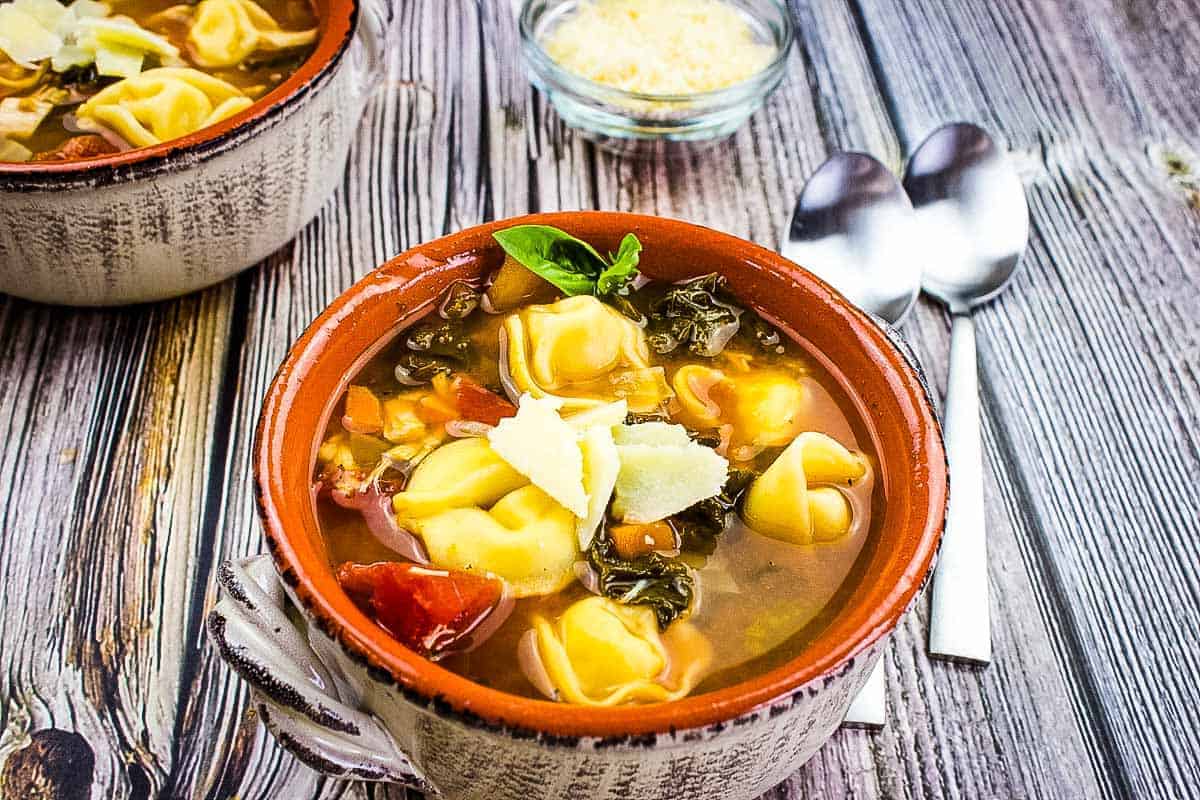 Kale and tortellini soup in a bowl on a wooden table.