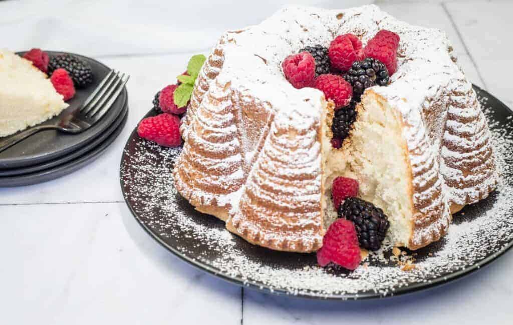 A powdered whipped cream cake garnished with raspberries and blackberries sits on a black plate.