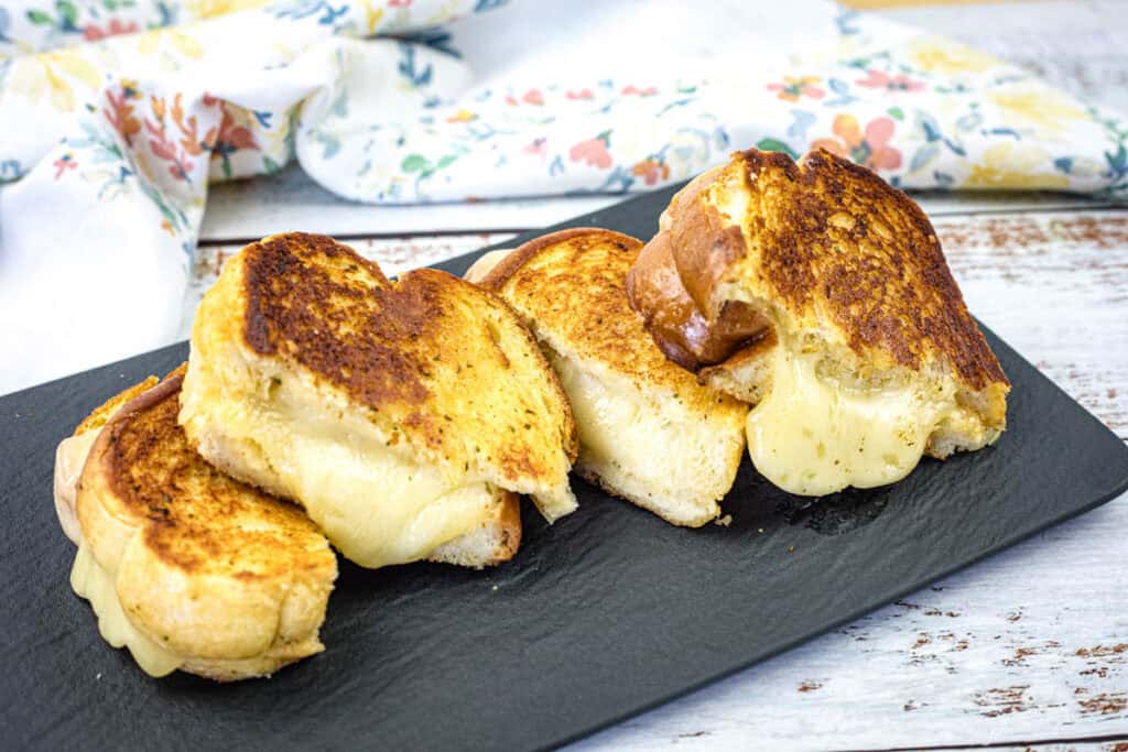 Four pieces of Garlic Bread Grilled Cheese on a black slate plate.