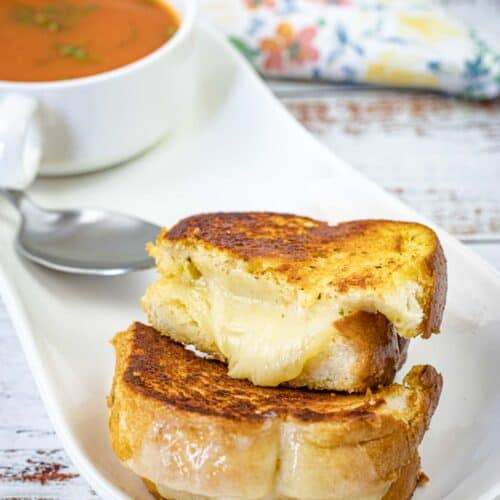 Garlic Bread Grilled Cheese with a bowl of soup beside a white plate.