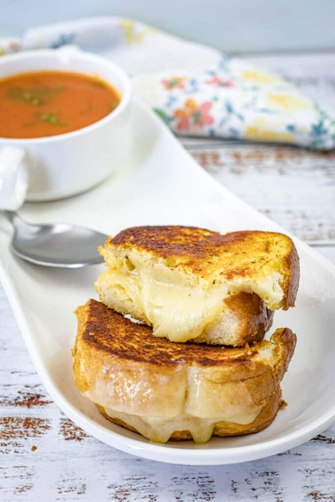 Garlic Bread Grilled Cheese with a bowl of soup beside a white plate.