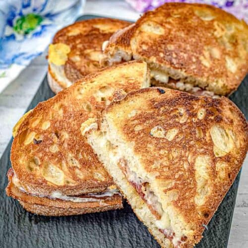 Halves of Bacon Grilled Cheese Sandwiches with Hot Honey Butter on a black slate plate,