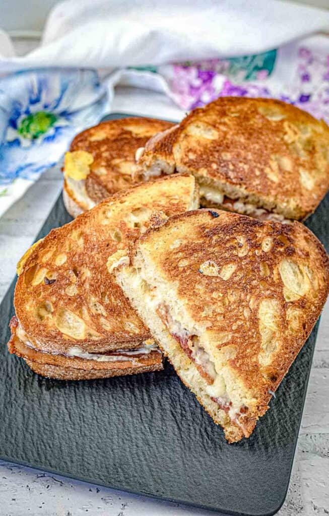 Halves of Bacon Grilled Cheese Sandwiches with Hot Honey Butter on a black slate plate,